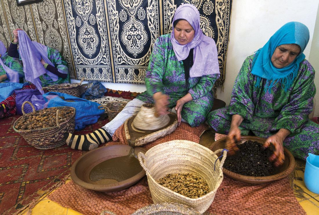 Women in headscarves seated on moroccan rugs process seeds