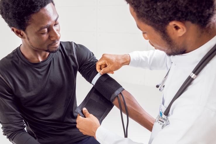 Black man has a blood pressure monitor fitted by Black doctor.