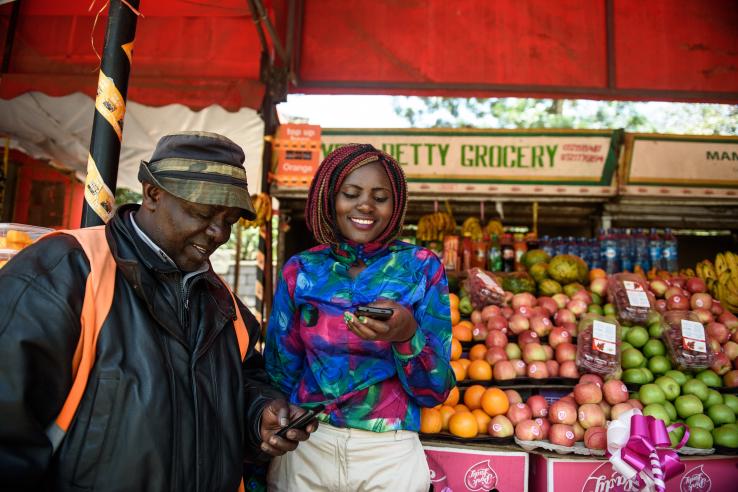 A man and a woman at a market looking at mobile phones