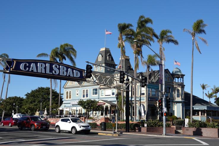 A street in Carlsbad, California, with a large sign reading "Carlsbad", cars waiting at a traffic light and a Victoria-style building in the background