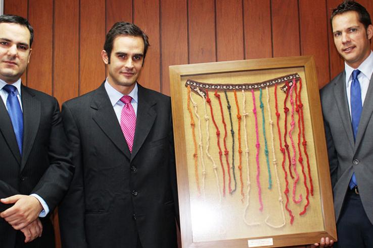 Three men in suits hold framed quipu