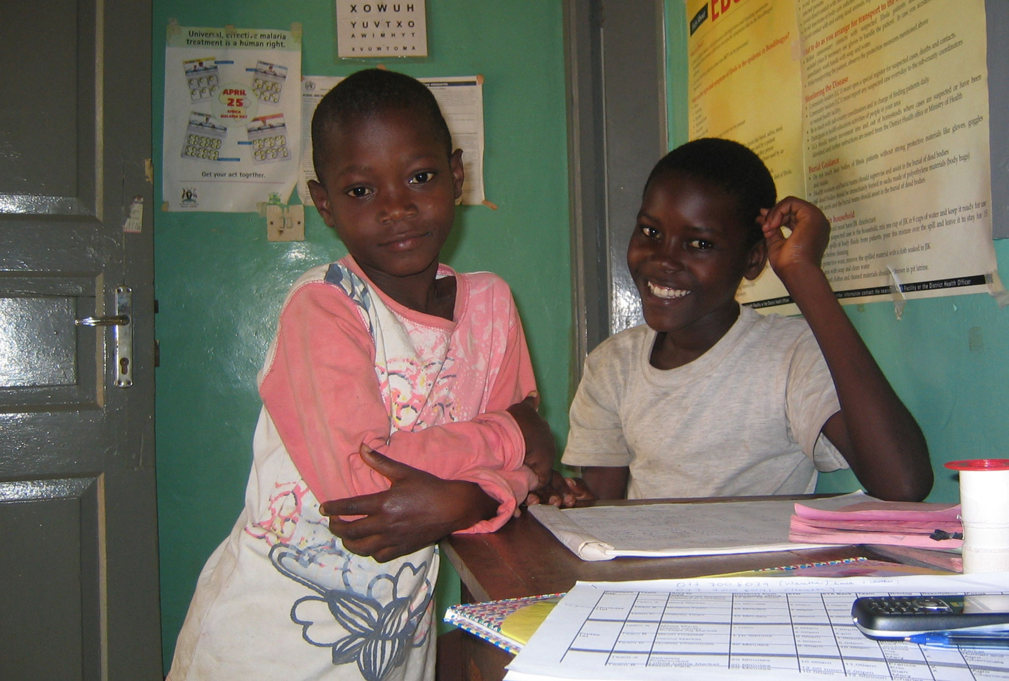Two Ugandan boys smile in a room filled with posters