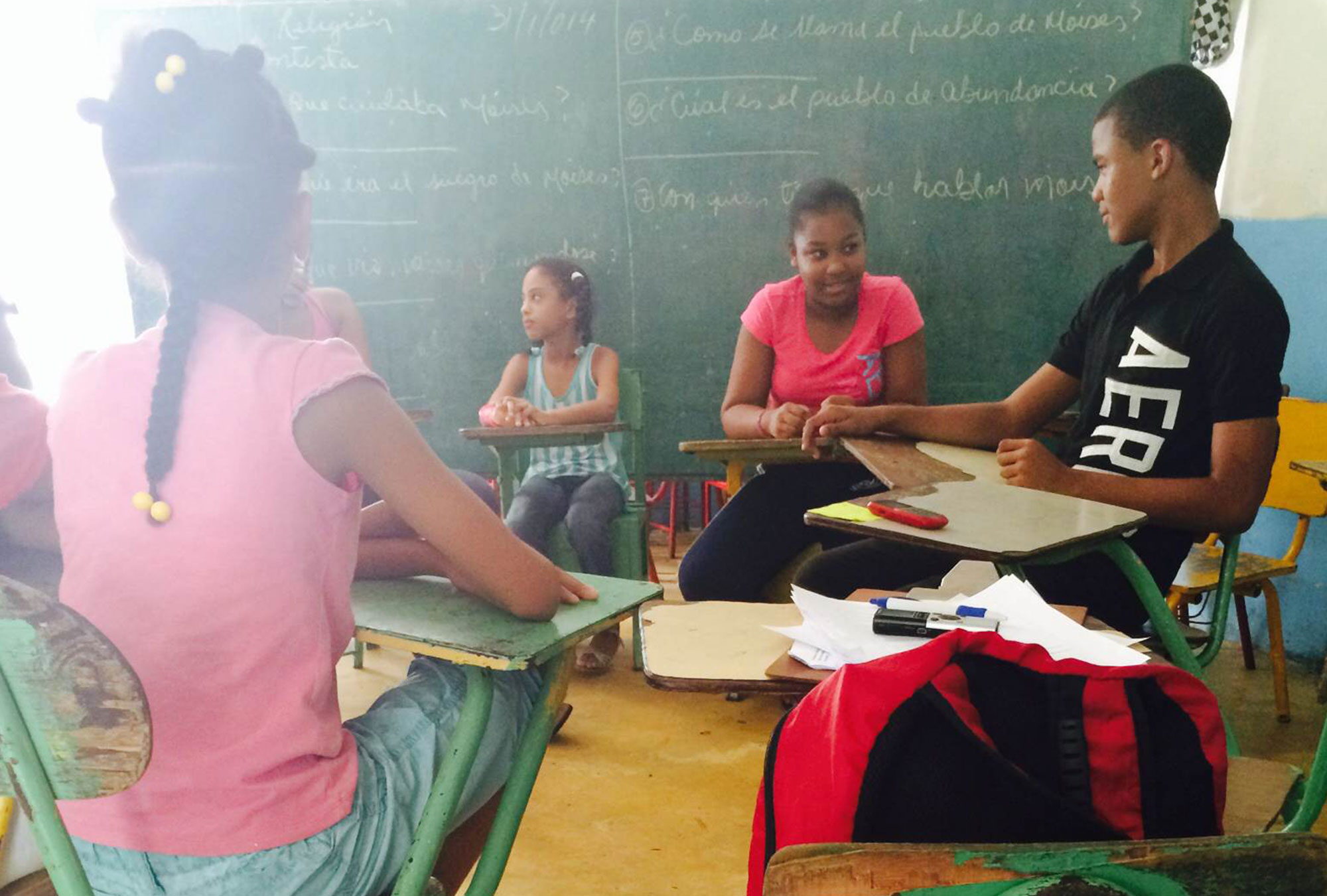 Children sit in schooldesks in front of blackboard