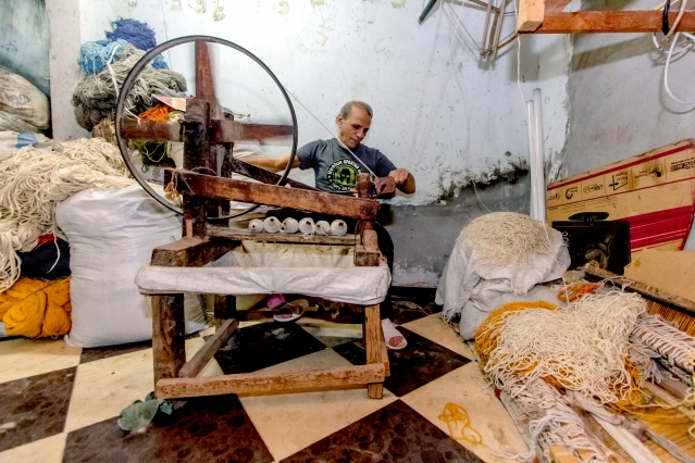 Man using spinning wheel next to piles of thread