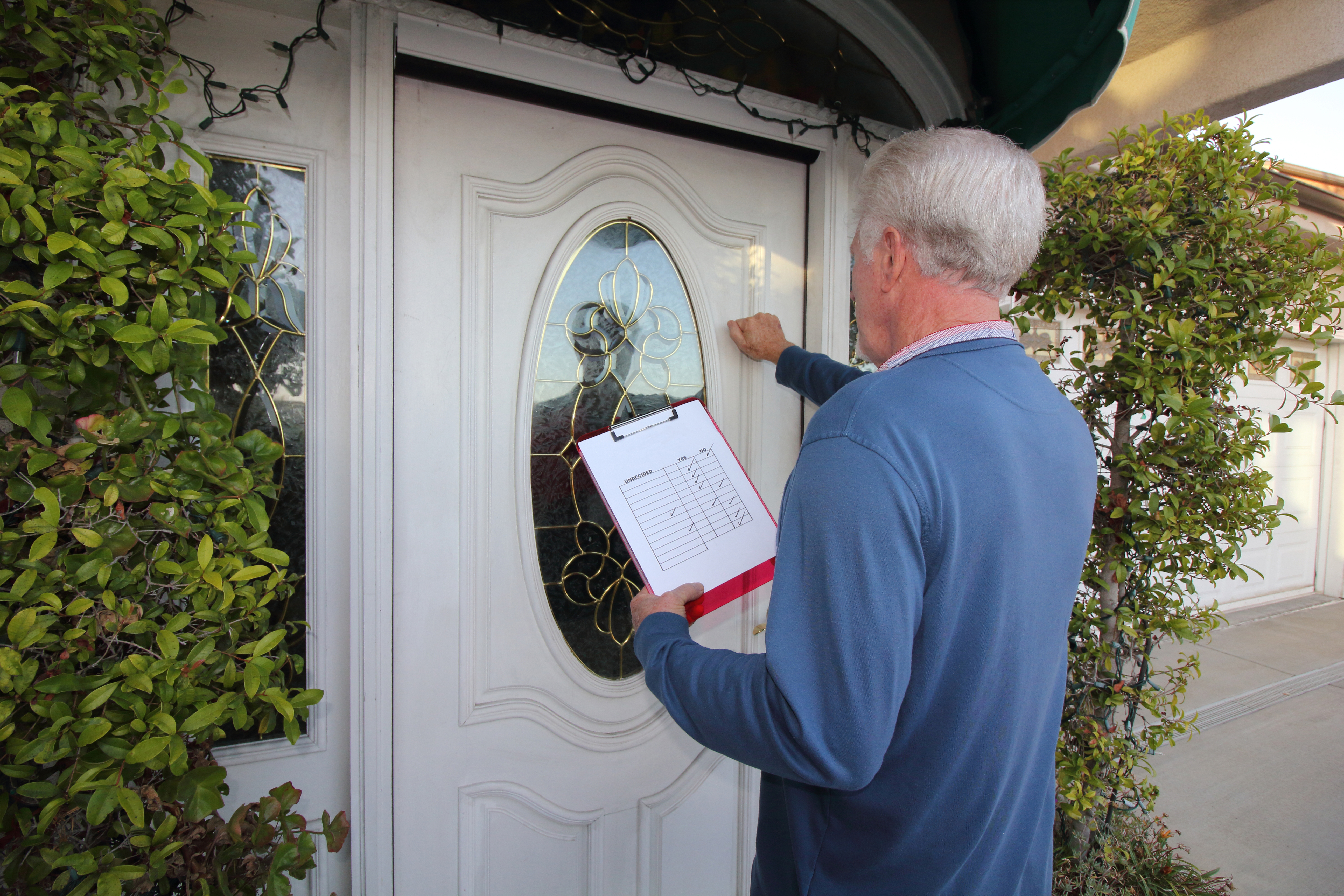 Man knocking on a door with a clipboard canvassing a neighborhoodl