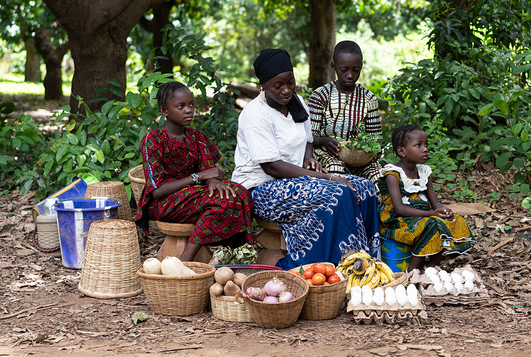 Woman with adolescent girls sit by road selling produce