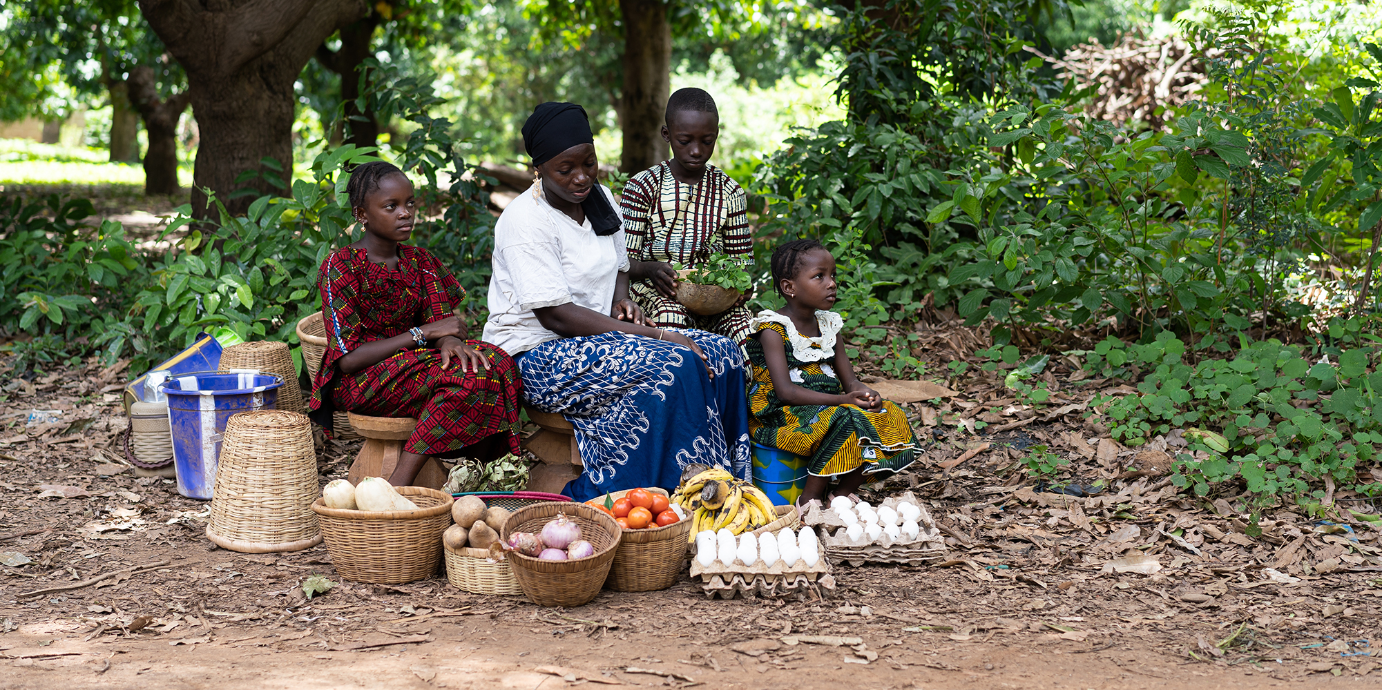 Woman with adolescent girls sit by road selling produce