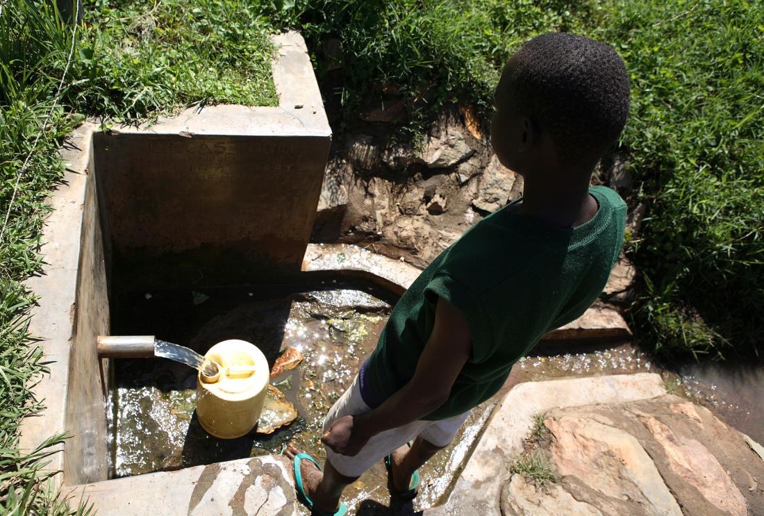 Boy watching water pour out of a concrete-encased spring.