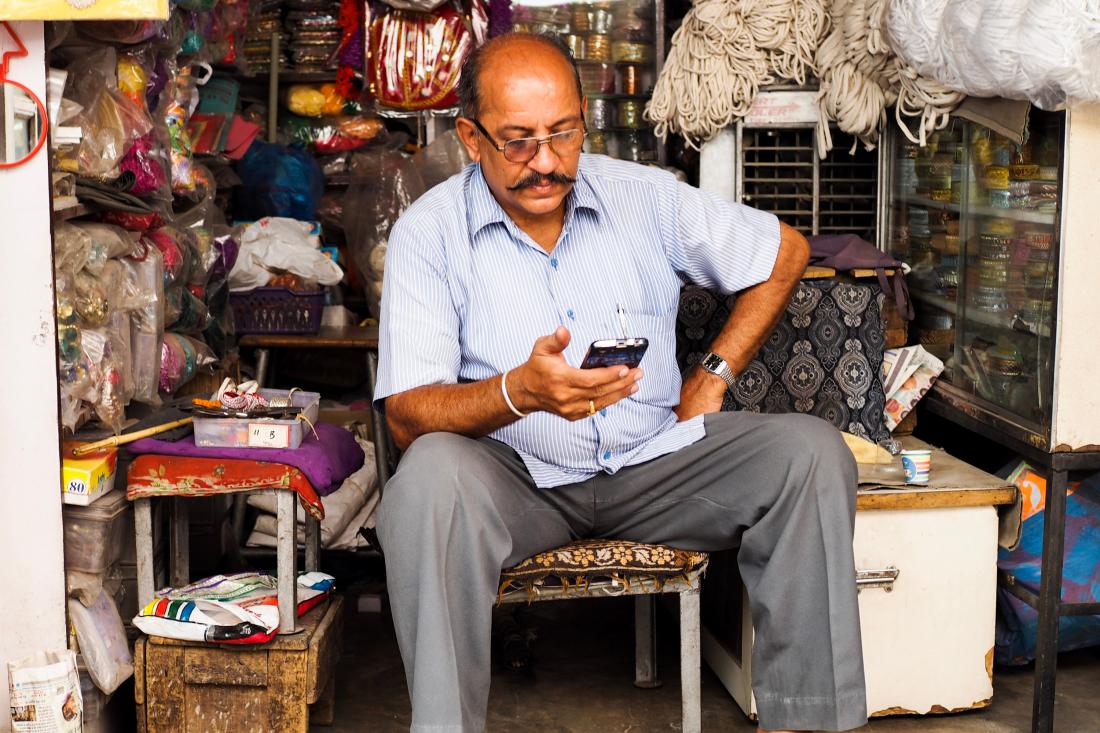 Indian man sitting on a stool looking at his cell phone