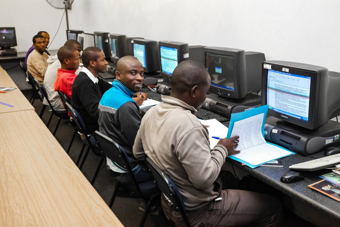 Seven South African men sit in a line at individual computers.