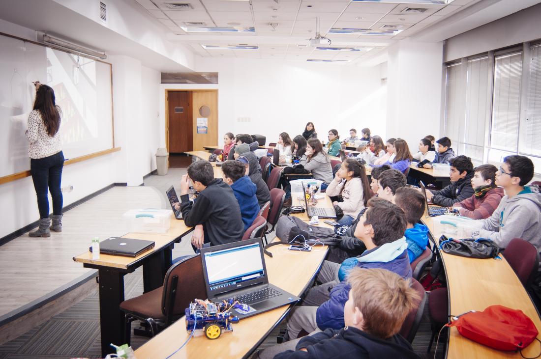teacher facing a white board and students sitting behind her in a classroom
