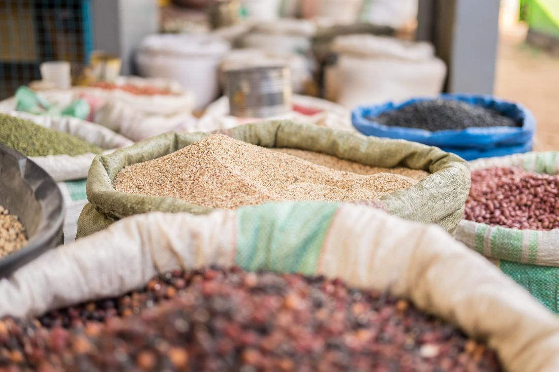 image focuses on one wholesale sack of grain and shows several grains behind it in an open air market setting
