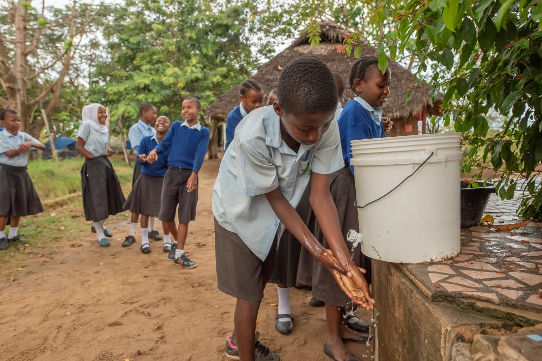 A boy washes his hands while other students are waiting in line for their turn