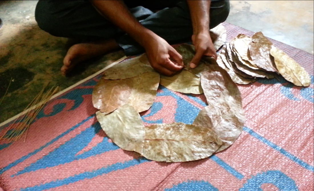 Two hands are seen stitching together leaves to form a plate