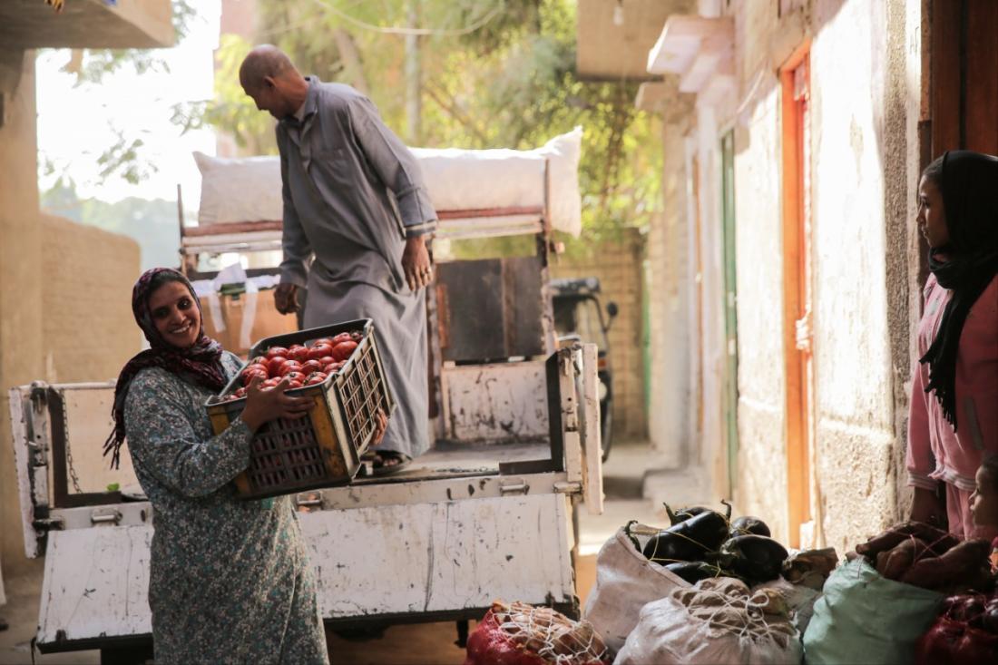 A man and a woman unload crates of vegetables off a truck