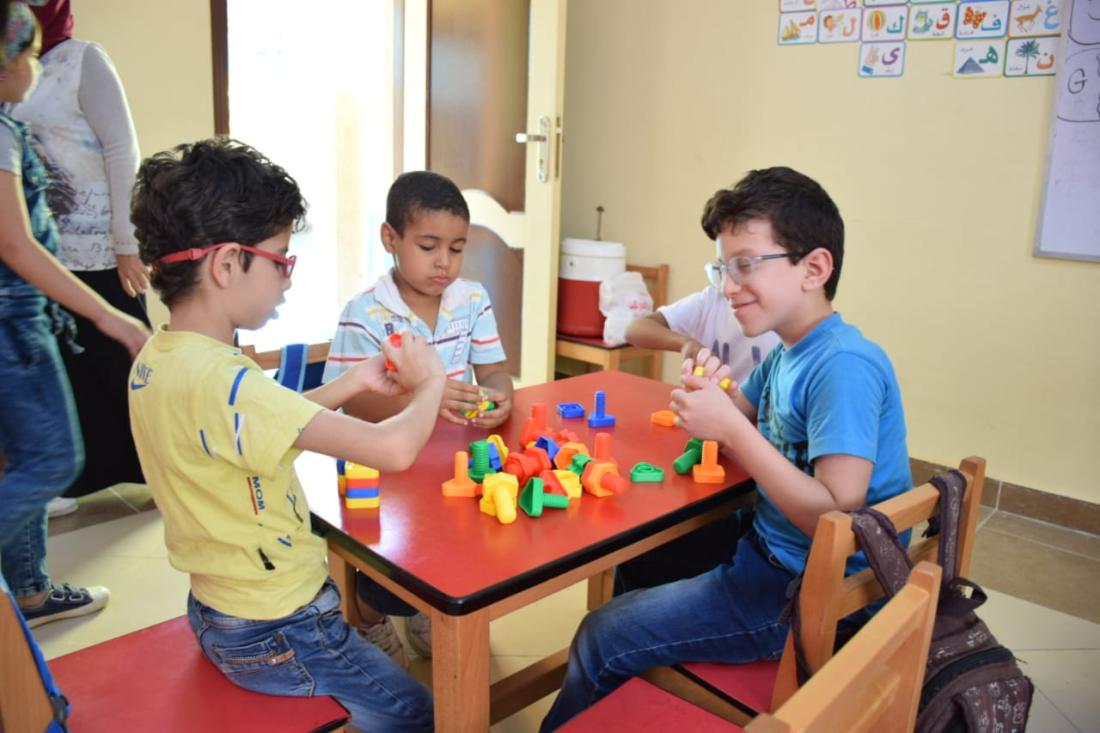Three young boys sit at a table playing with pegs