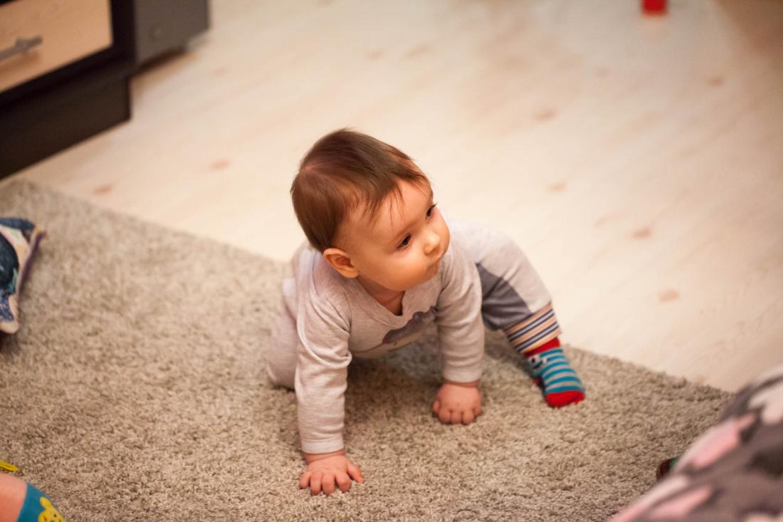 A infant on a rug is the in process of standing up from all-fours.
