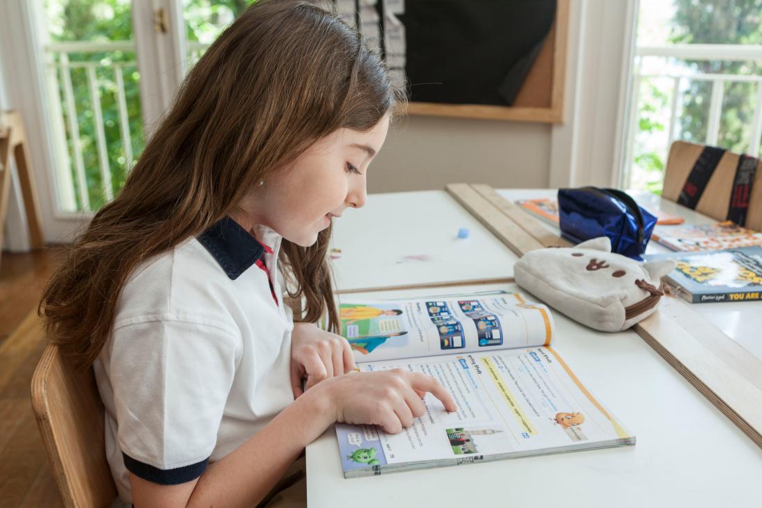 A girl sits at her desk reading a textbook.