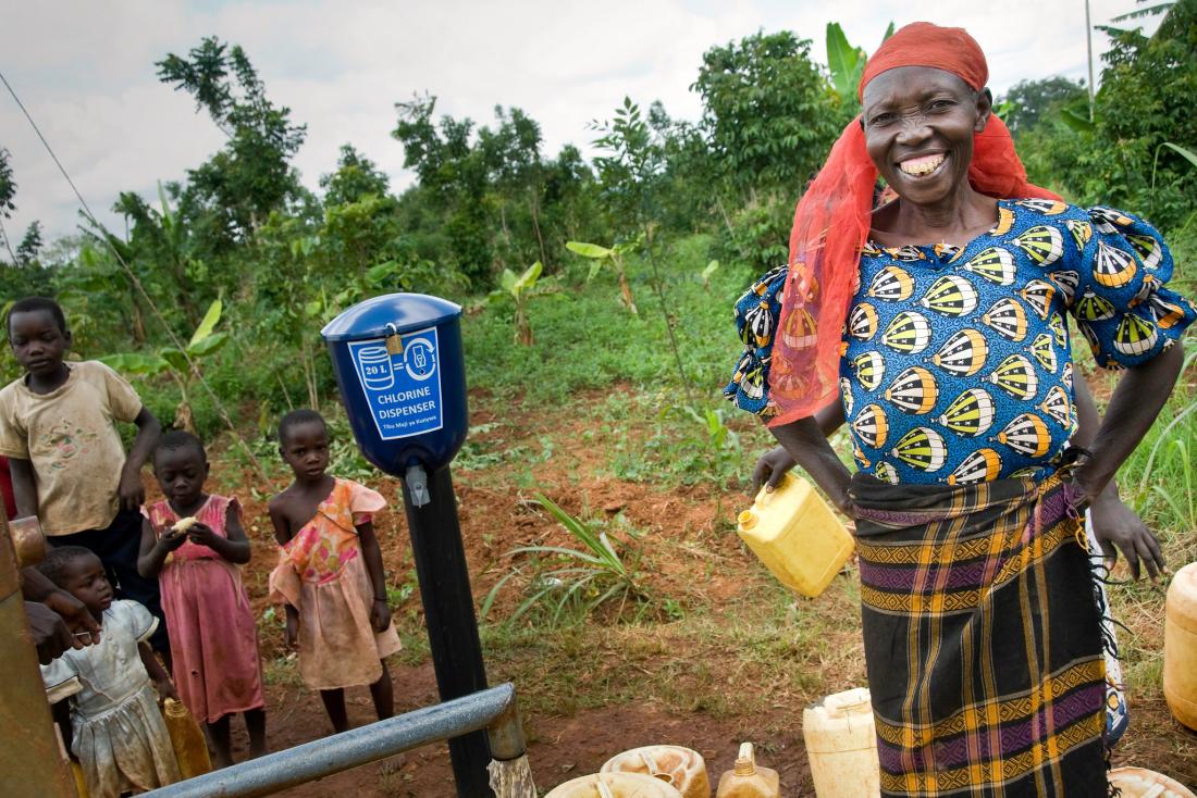 A woman and children are standing next to a chlorine dispenser installed at a water source in a village in Kenya.