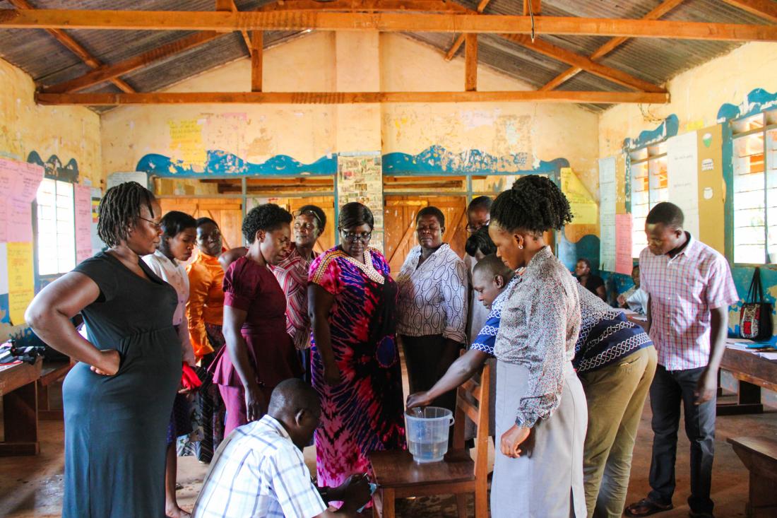 Teachers gather in a circle around a table with a bucket of water