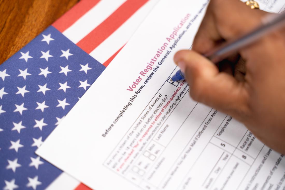 A person fills out a voter registration form on a table with an American flag.