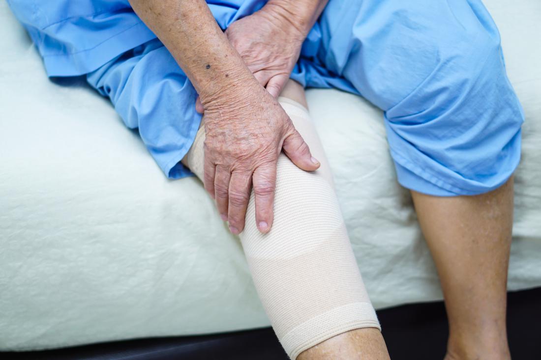 A patient holds their knee, which is wrapped in a recovery bandage, after surgery.