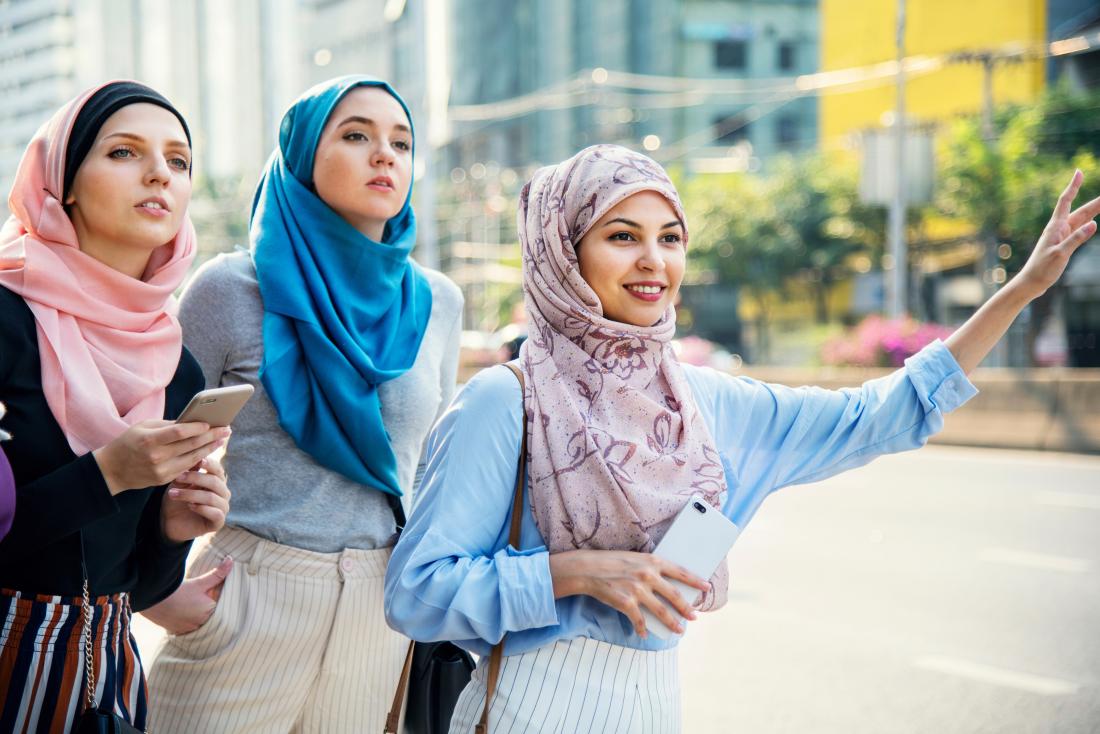 Women stand at a curb hailing a cab or rideshare car