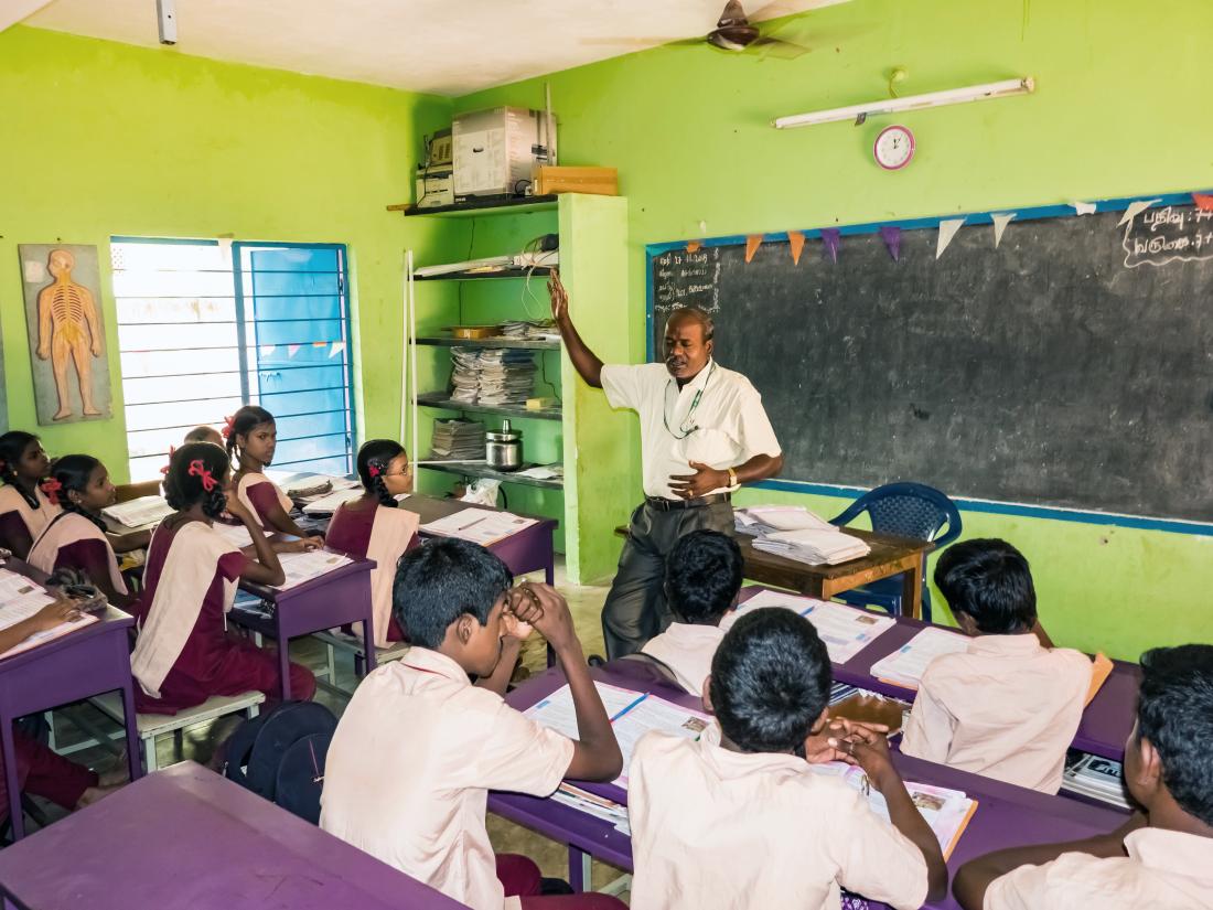 Image of a teacher at a blackboard in front of a class of students in India.