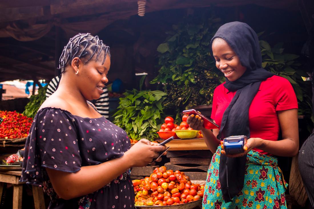 Two women use mobile money to complete a transaction.