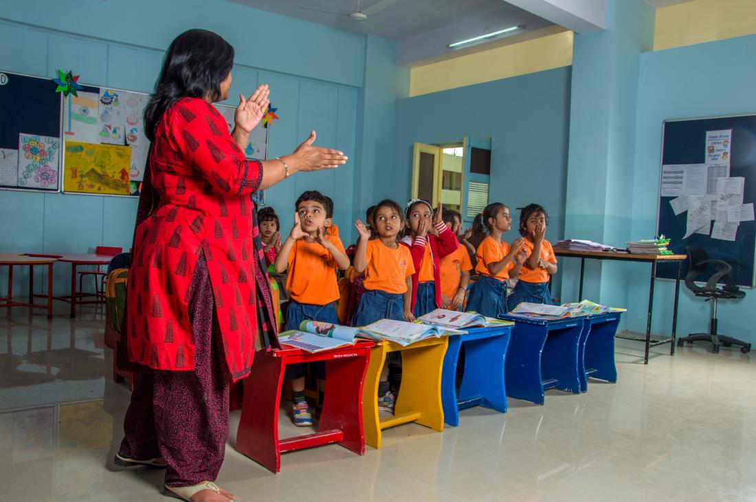 Female teacher standing in front of young students using her hands to describe a concept