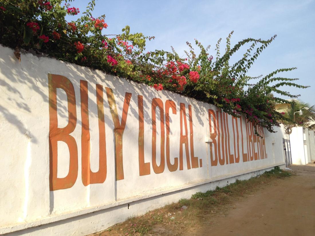 Street wall with words painted in orange reading "buy local build Liberia"