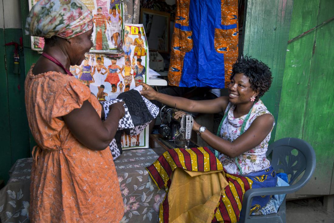 Seated woman showing pieces of cloth to another woman