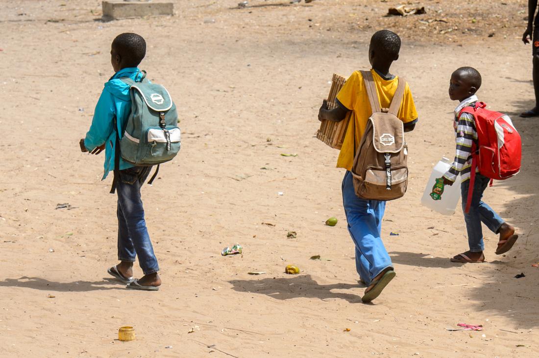 Three primary school students with backpacks walking on street