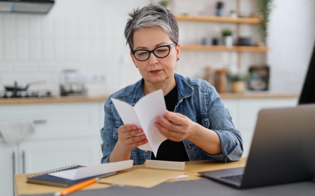 A middle-aged woman with short hair and glasses reads a fundraising letter from a German charity