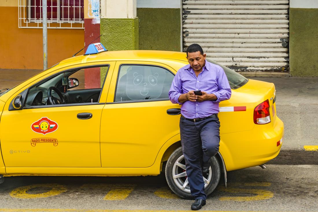 Man looking at text messages leaning on yellow car in Ecuador