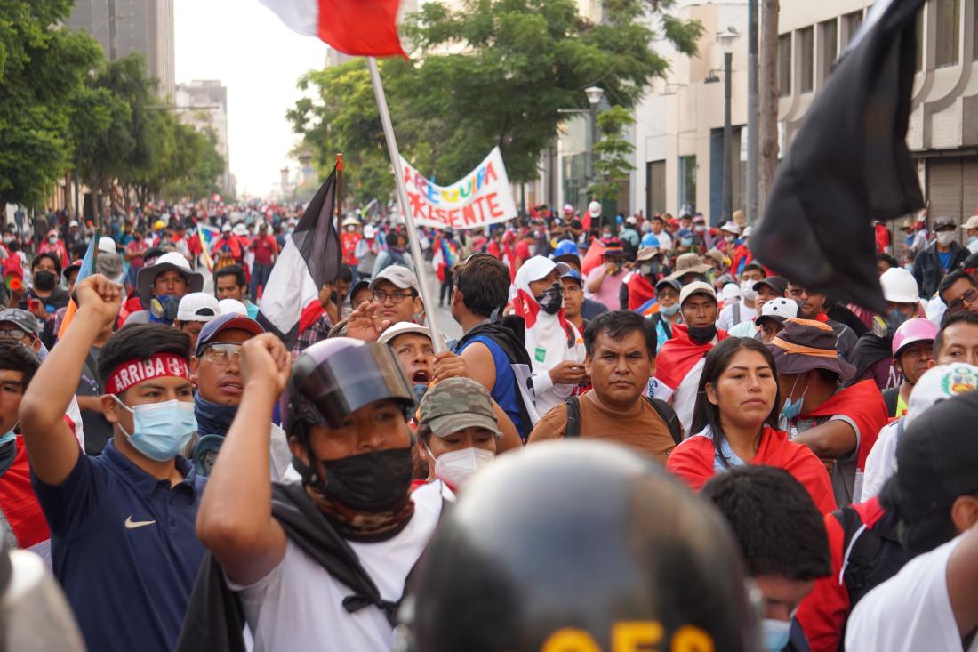 A crowd of people, many wearing red, engaging in political protest on streets in Peru