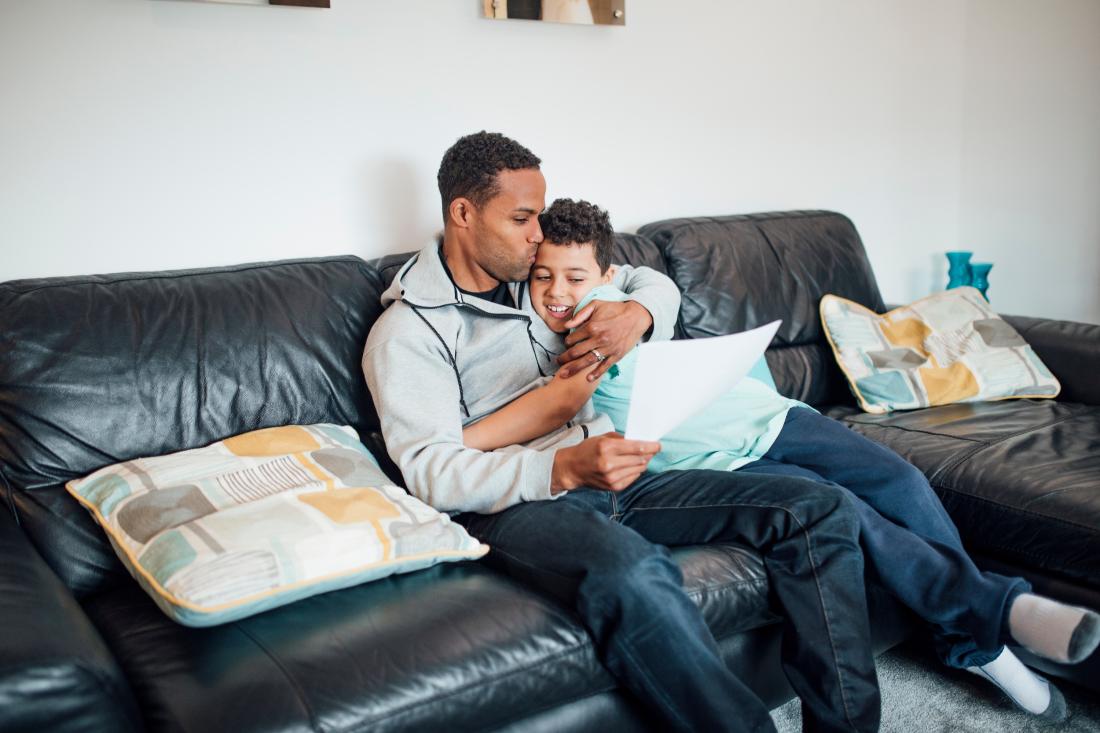 Father hugs son on couch while looking at his student performance records in Malawi