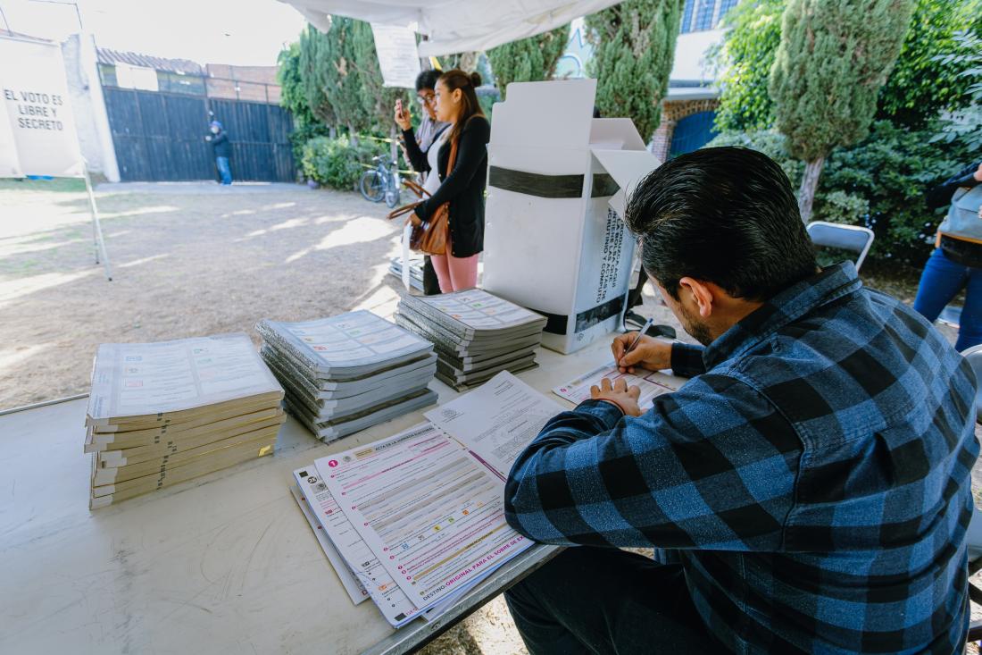 Male poll worker in blue-checkered shirt donating time to participate in electoral term
