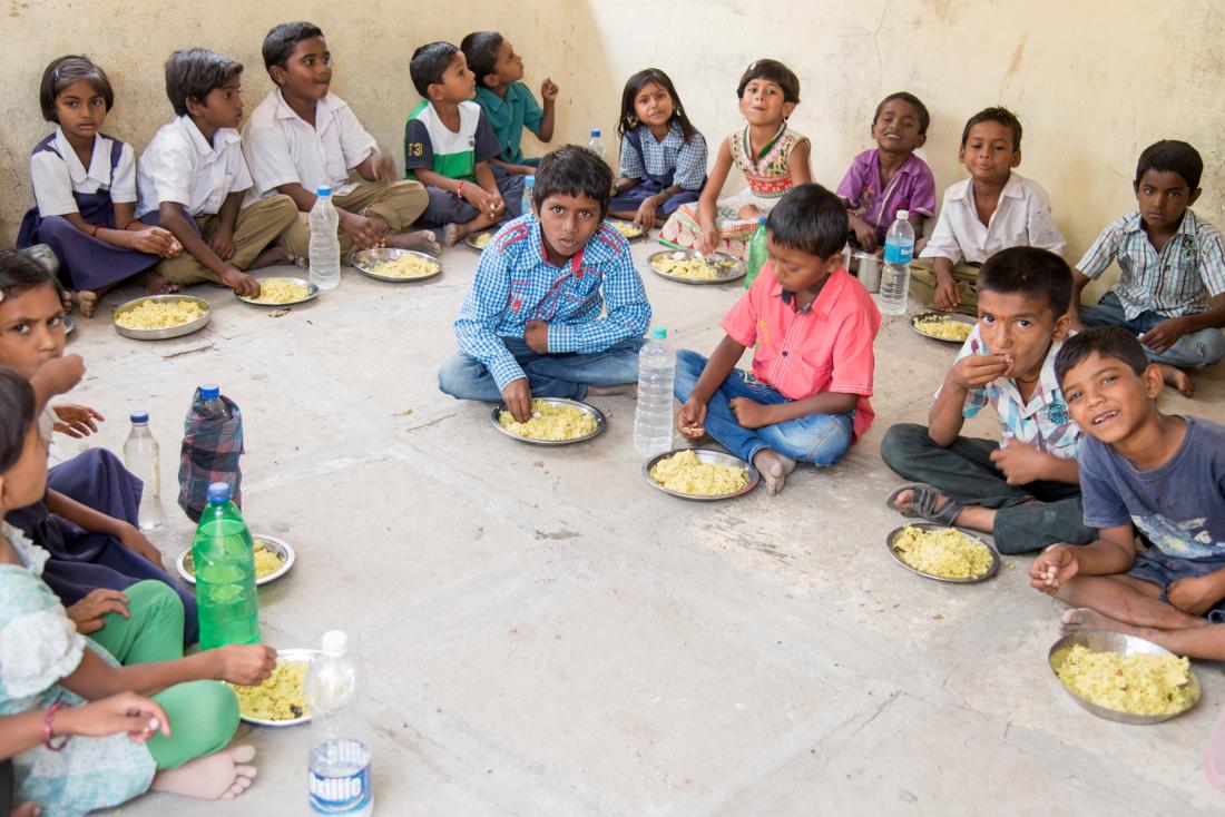 Group of school children eating meals from school-based nutrition program in India
