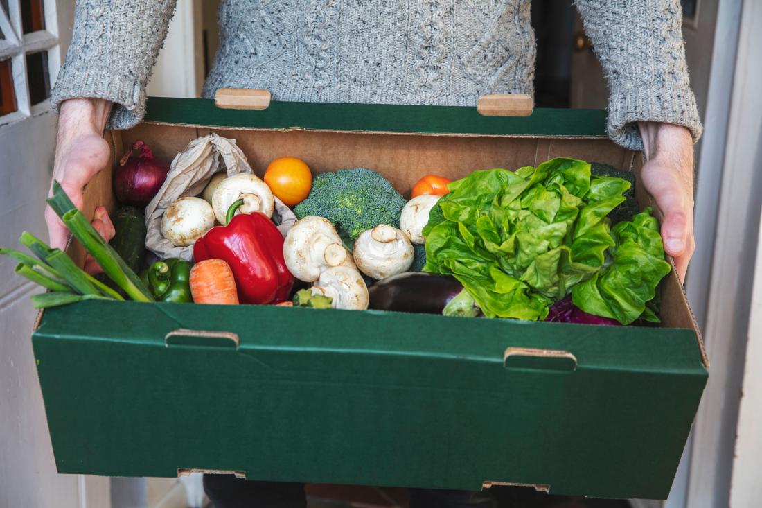 A person picks up a box of fresh vegetables.