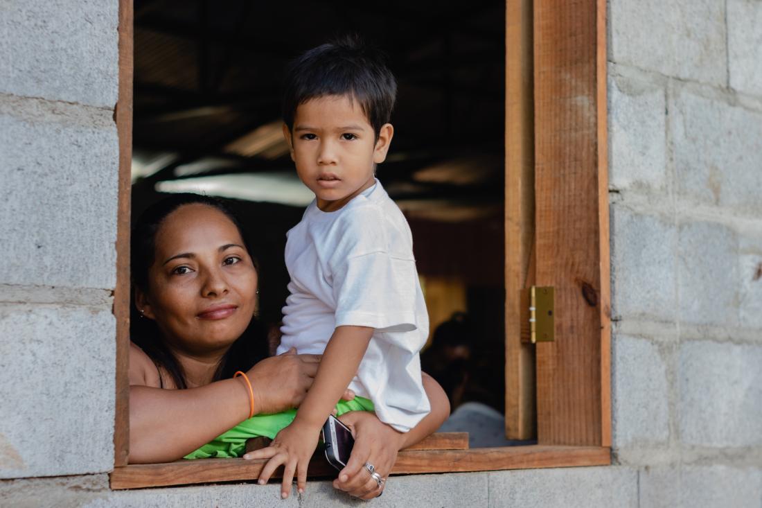A woman and child look out from a window of a concrete home in Nicaragua.