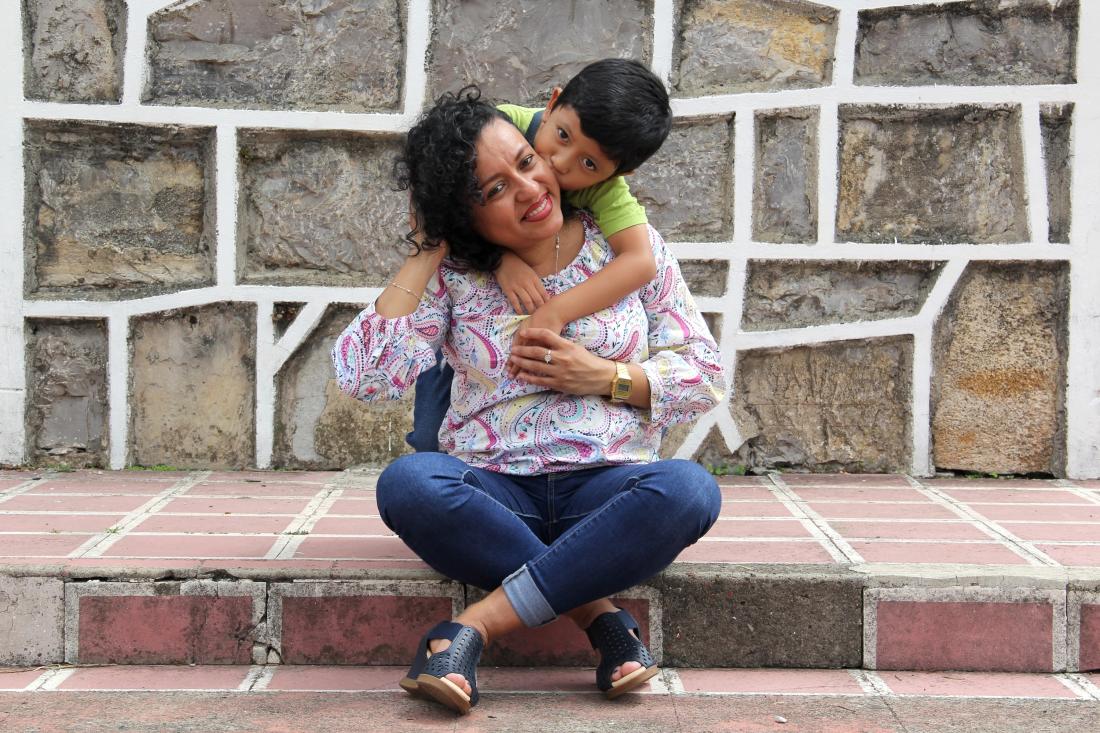Seated mother with short curly hair being embraced by elementary school aged boy from behind in Chile