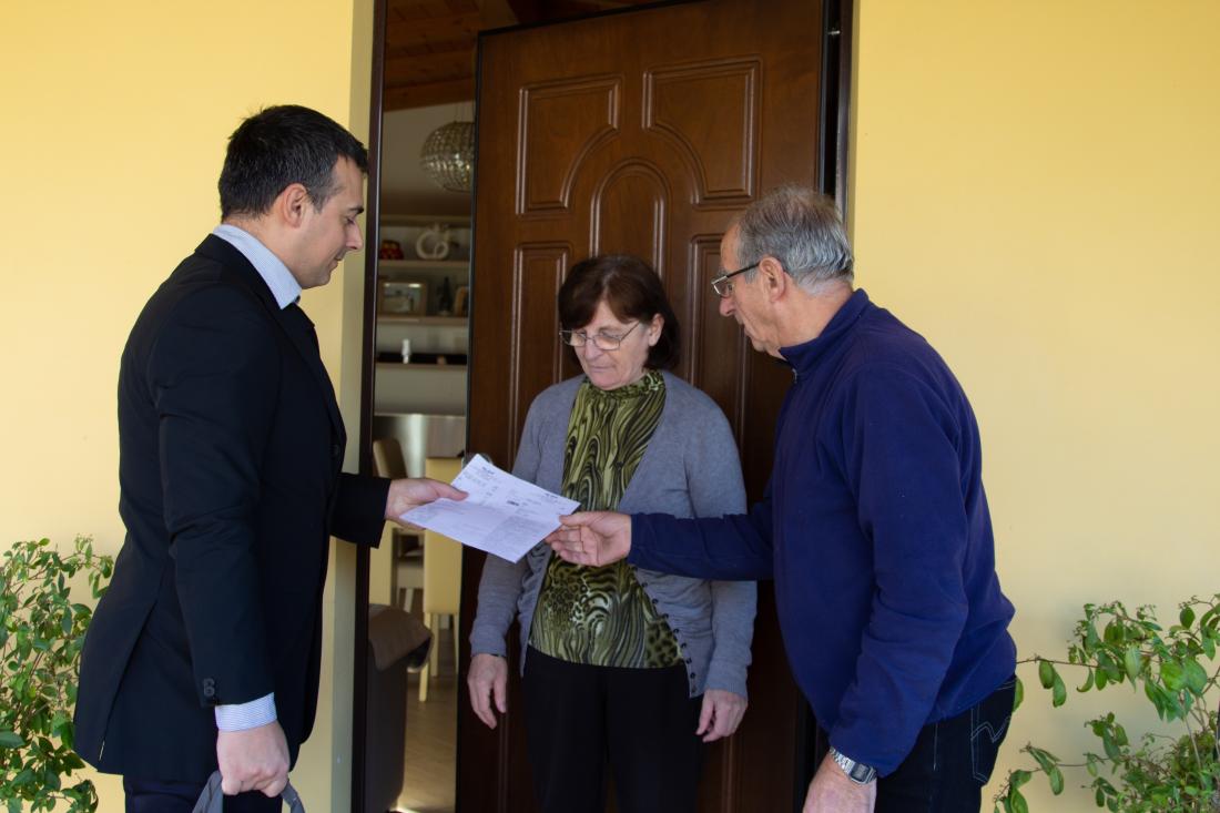 A male canvasser speaks to couple in front of door for votes in local election in the United States.