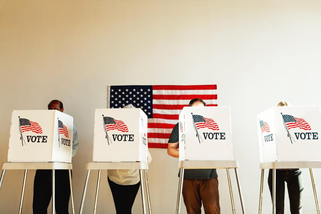 Voter participation with people behind voting booths in the United States with American flag in background