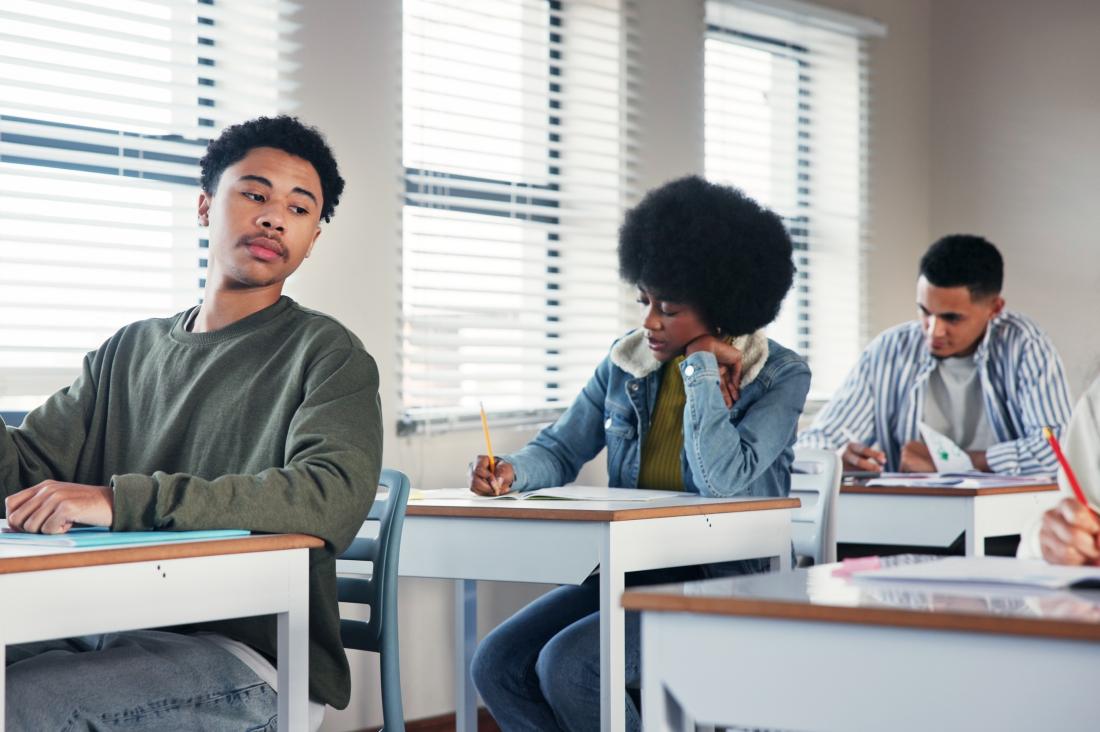 Student plagiarising on school exam by looking over at another student's paper in classroom setting in the United States