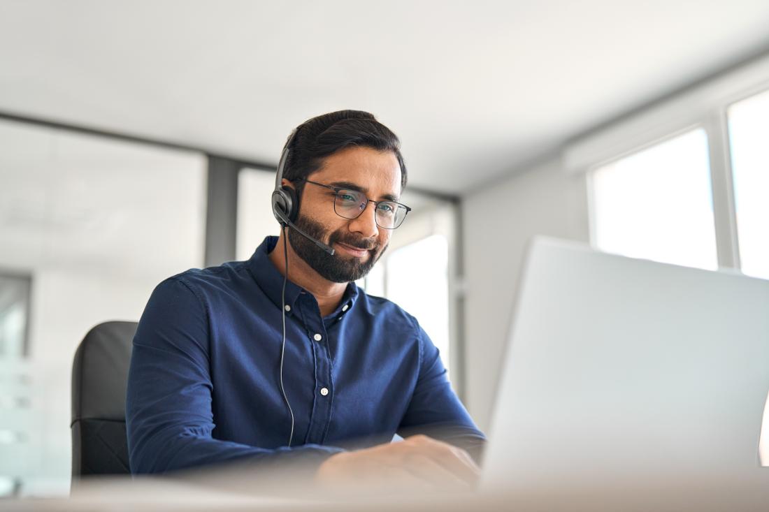 Man with glasses and dark hair looks at computer screen while speaking into headset building relationship with bank client
