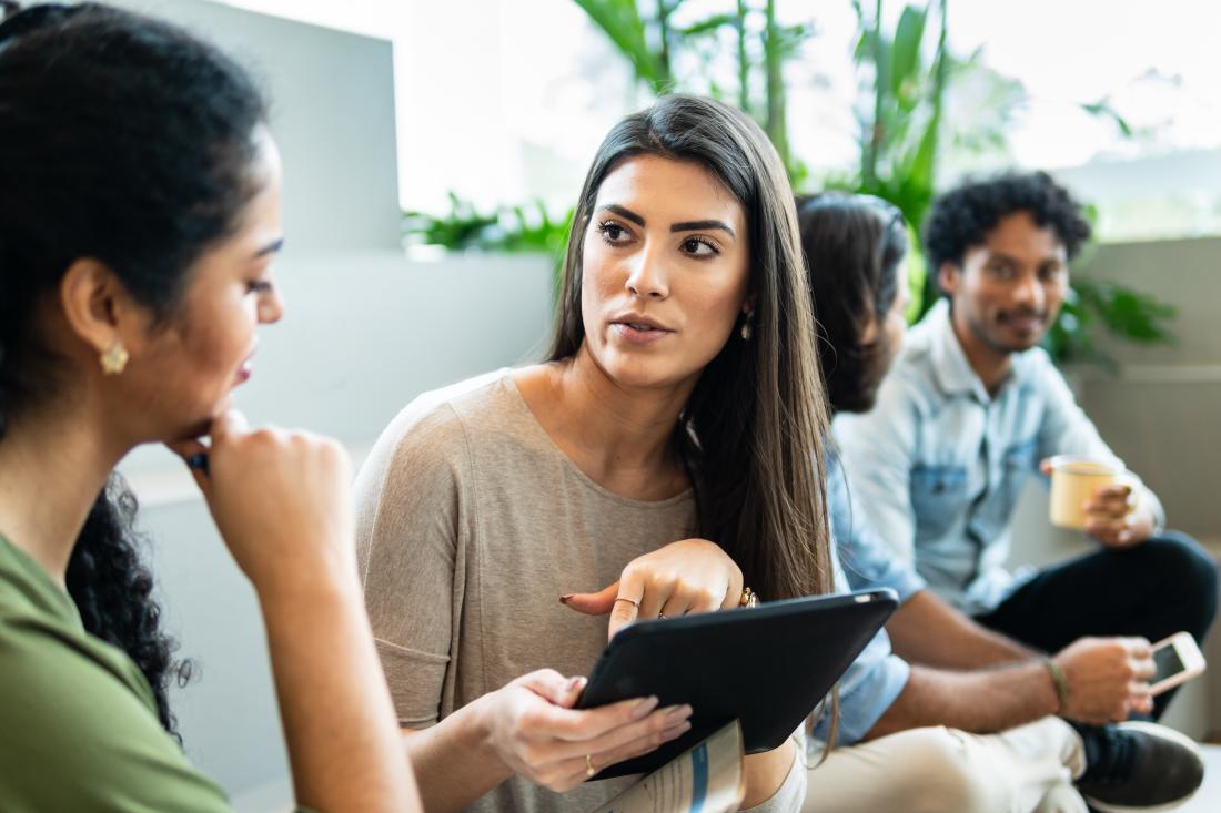 Woman with long straight hair points to tablet and talks to friend about financial decisions in Brazil