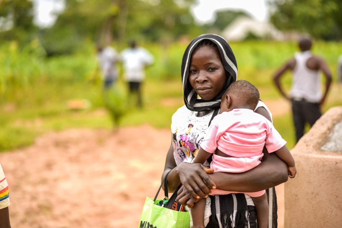 A mother carries her child in her arms outdoors in Nigeria.