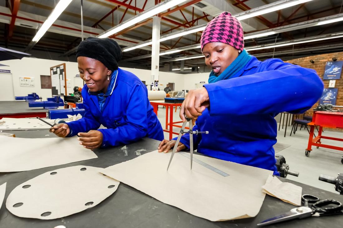 Two firm-worker women in blue sweaters and hats work on project at training facility