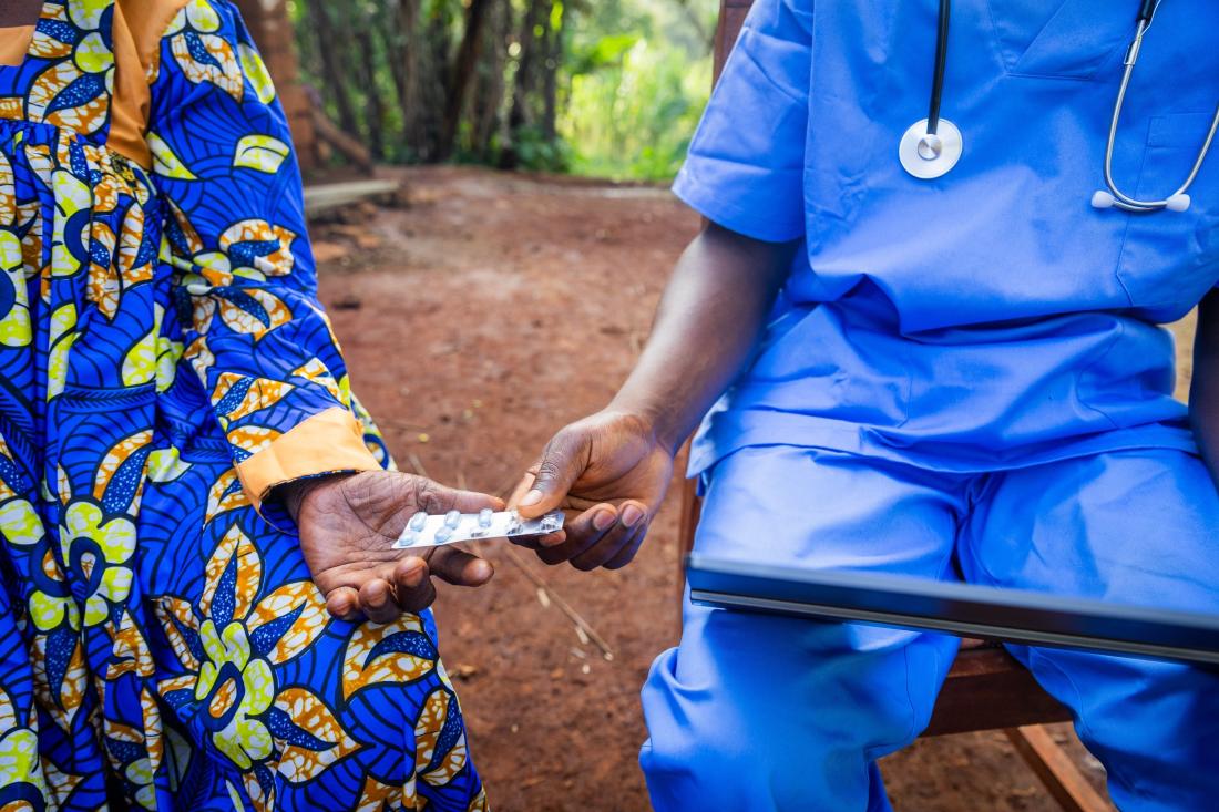 Doctor with blue uniform hands malaria treatment medication to patient in Uganda